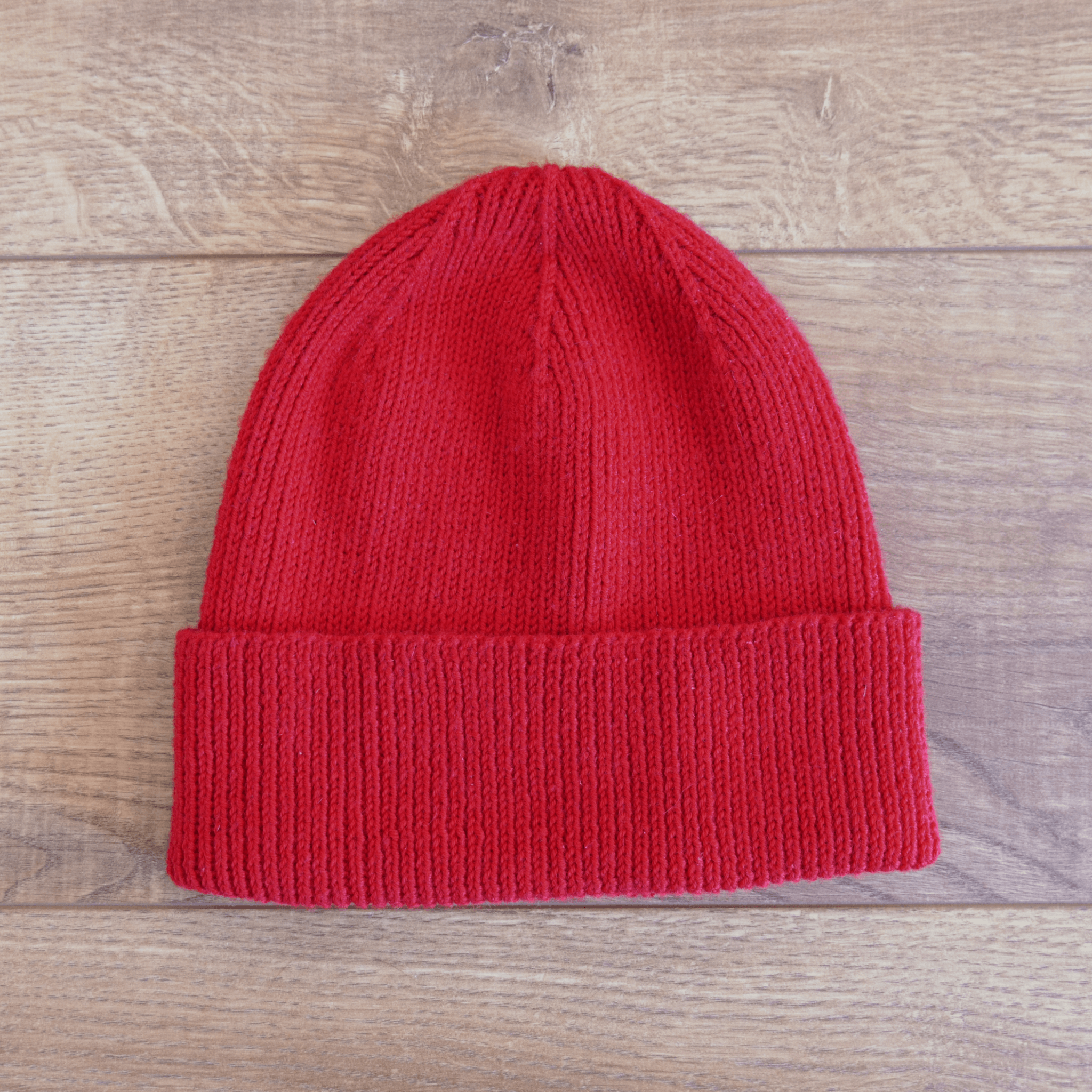 Bright red knit beanie laying flat on a wood floor