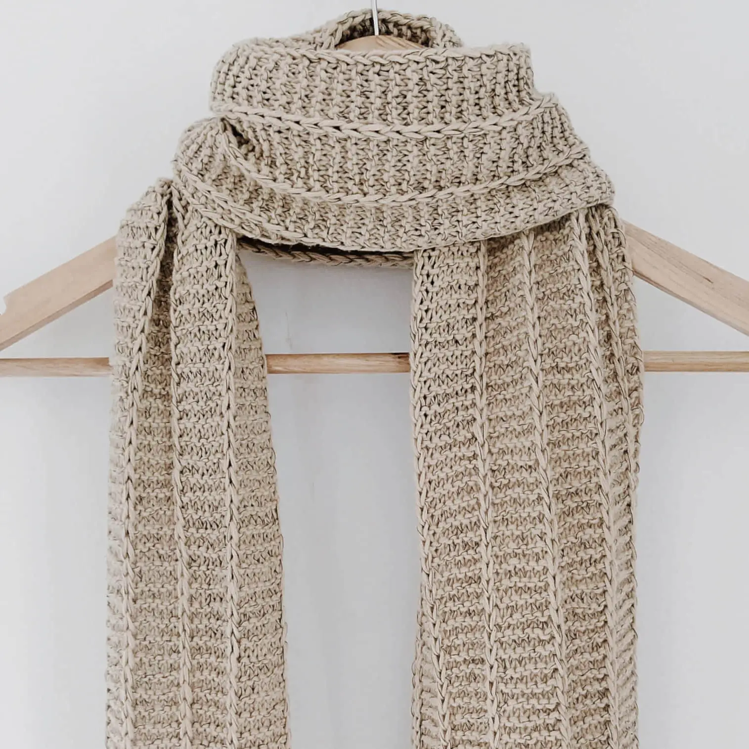 The father-in-law scarf by KnitQ hanging on a wooden hanger in front of a white background