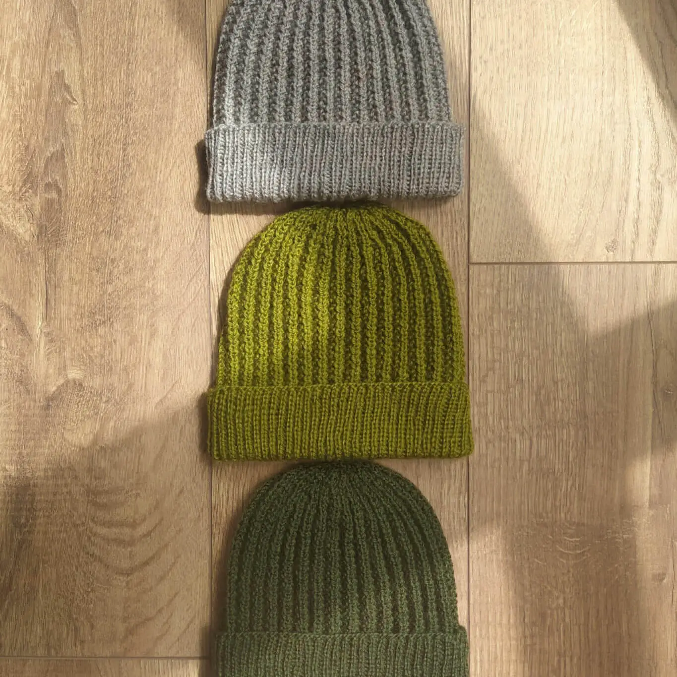Three one more mistake beanies stacked, with shadows stretching across