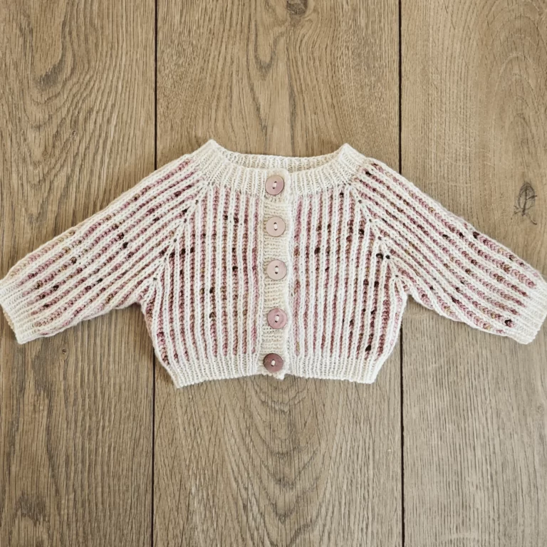 The marionberry newborn cardigan laid flat and buttoned on a wood backdrop