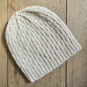 A flatlay photo of the single basketweave beanie on a wood backdrop
