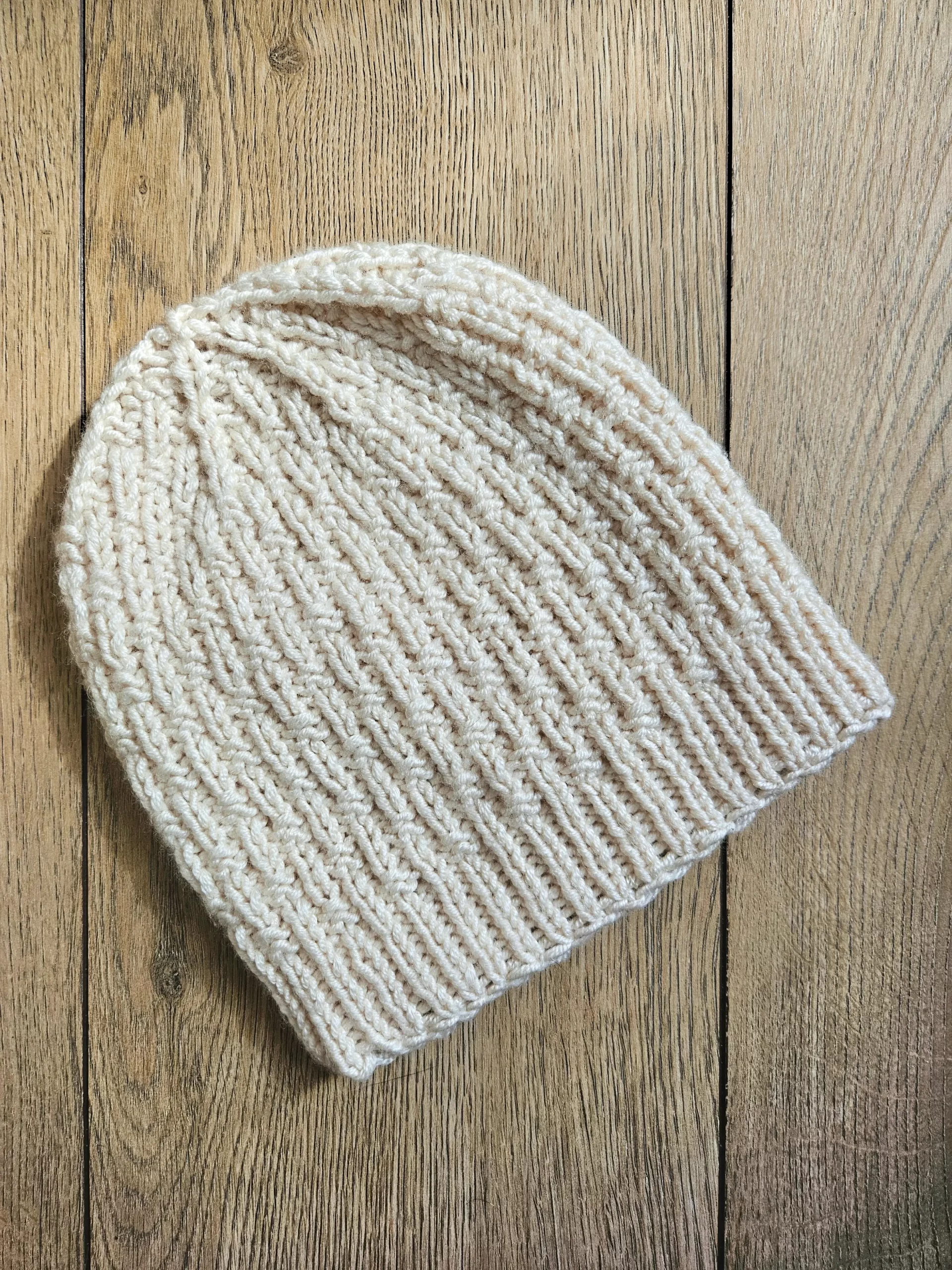 A flatlay photo of the single basketweave beanie on a wood backdrop